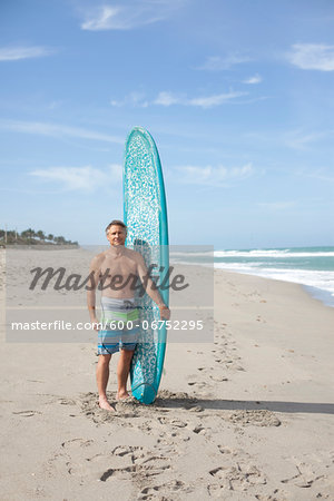Portrait of Mature Man with Surfboard on Beach, USA