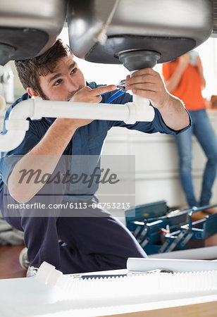 Plumber working on pipes under sink