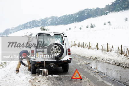 Man working on broken down car in snow