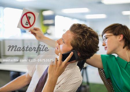 Businesswoman showing 'no cell phones' sign to colleague