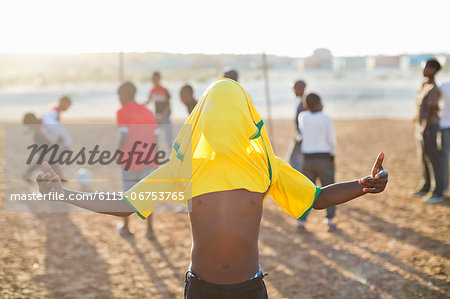 Boy celebrating with soccer jersey on his head in dirt field