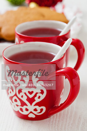 Christmas mulled wine in two small red cups and gingerbread and baubles on white background
