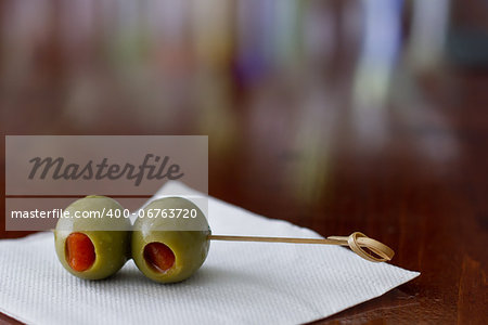 closeup of cocktail olives sitting on a white bar napkin with a shallow depth of field on a busy bar