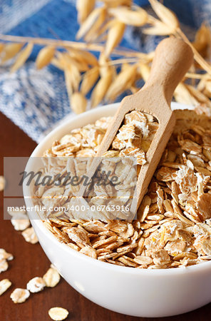 Oat flakes in a bowl witn wooden scoop close up.