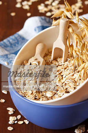 Oat flakes in a bowl with wooden scoop close up.