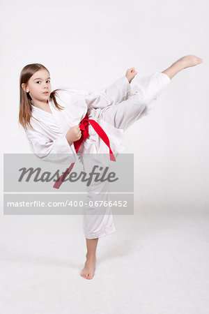 Karate young girl in a kimono with a red belt kicking up, isolated on white background