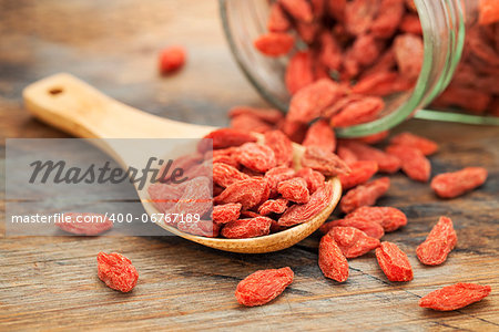 Tibetan goji berries (wolfberry) spilling of the glass jar on a wooden spoon, selective focus