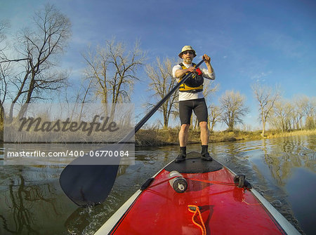mature male paddler on a red stand up paddleboard (SUP), calm lake in Colorado, early spring