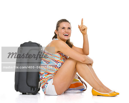 Young tourist woman with wheel bag sitting on floor and pointing on copy space