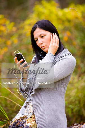 Woman wearing earbuds and listening to a smart phone outdoors