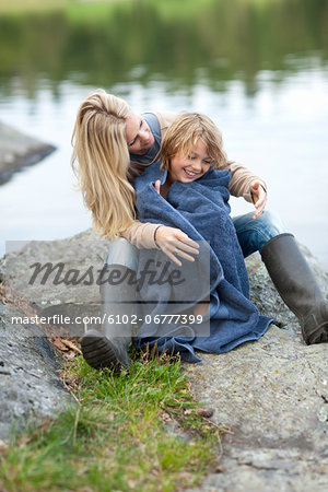 Mother drying son with towel at lake