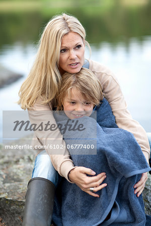 Mother drying son with towel at lake