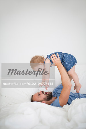 Man lying on bed and holding little daughter