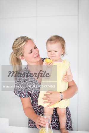 Little girl eating lemon while mother embracing her