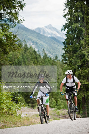 Two mountain bikers riding on road, Chiemgau, Bavaria, Germany