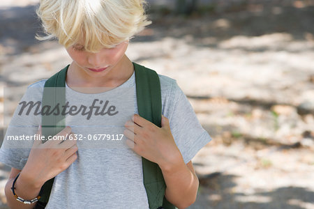 Boy wearing backpack, head down, portrait