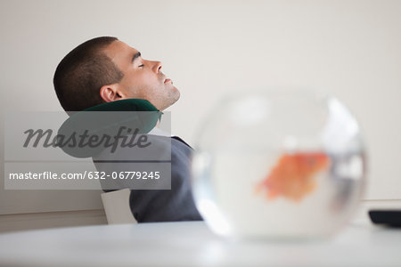 Businessman resting with neck pillow in office, side view