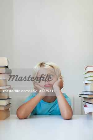 Boy sitting between tall stacks of books, bored expression on face