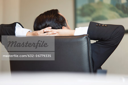 Business executive relaxing in office chair with hands behind head