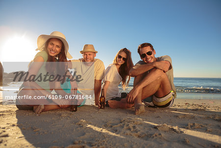 Smiling friends sitting on the beach with beers Smiling friends sitting on the beach with beers