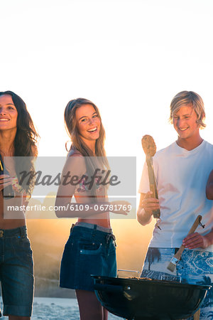 Smiling friends cooking barbecue on the beach