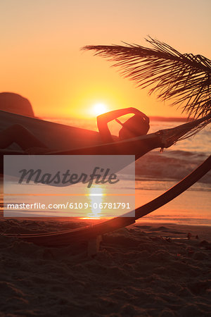 A person wearing a straw hat and relaxing in hammock on the beach