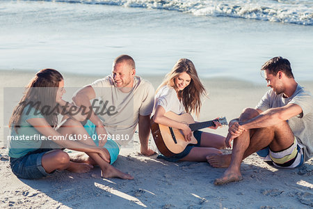 Friends sitting on the sand playing guitar