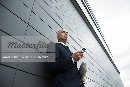 Portrait of businessman leaning against wall of building, holding cell phone, Mannheim, Germany