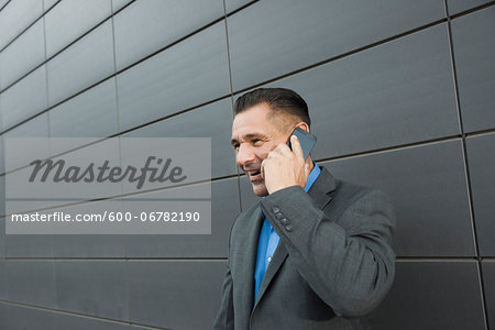 Close-up portrait of businessman standing in front of wall of building using cell phone, Mannheim, Germany