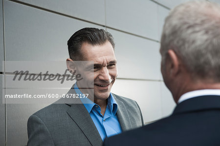 Mature businessmen standing in front of wall, talking