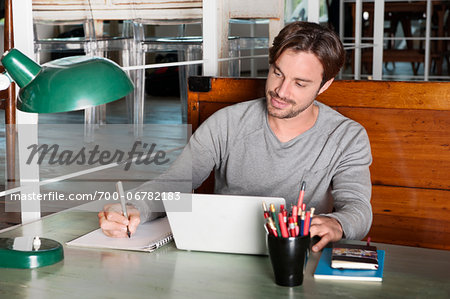 Man with Laptop Writing in Notebook