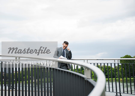 Mature businessman standing on bridge looking at documents, Mannheim, Germany
