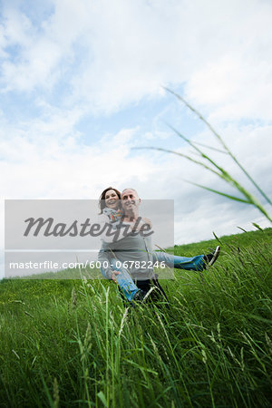 Mature couple in field of grass, man giving piggyback ride to woman, Germany