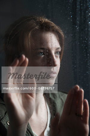 Teenage girl looking out with hands on window, wet with raindrops