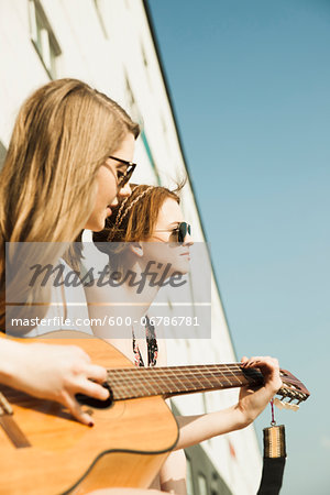 Young women sitting outdoors, hanging out and playing guitar, Mannheim, Germany