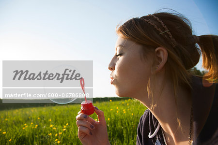 Close-up of teenage girl blowing bubbles in field, Germany