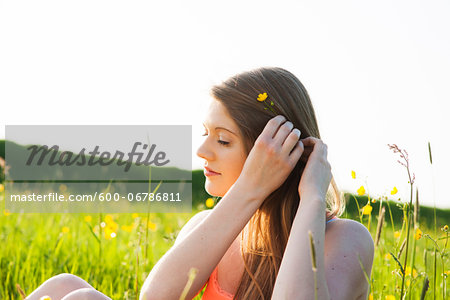 Young woman sitting in field placing flower in hair, Germany