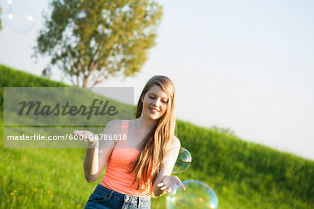Young woman standing in field playing with bubbles, Germany