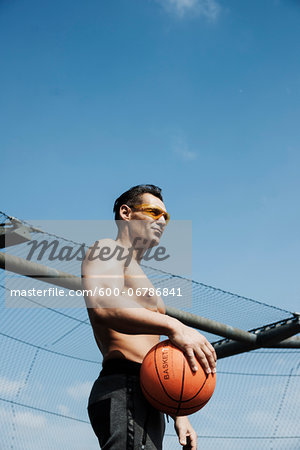 Mature man holding basketball, standing on outdoor basketball court, Germany