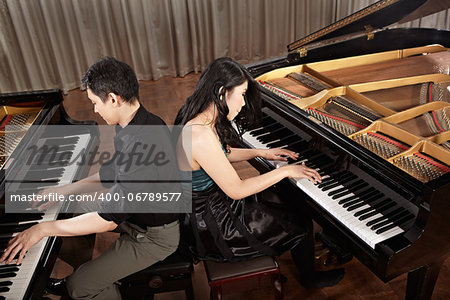 Two people, a couple playing duet musical performance with two grand pianos