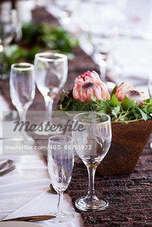 Wine and champagne glasses on a table with protea flowers and a pot