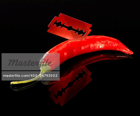 studio shot of a sharp razor blade and red hot chili in dark reflective back