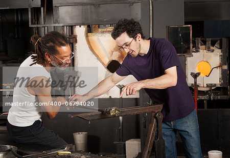 Two glass artisans working together on small vase