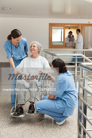 Old woman in wheelchair talking with nurses in hospital corridor