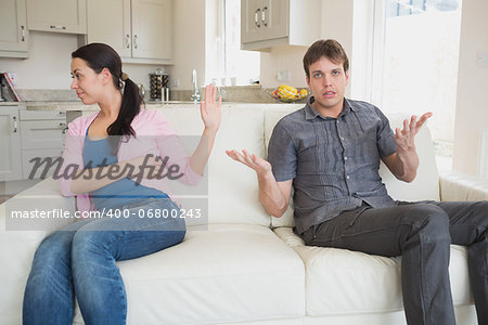 Two people sitting on the couch in the living room while waving each other away