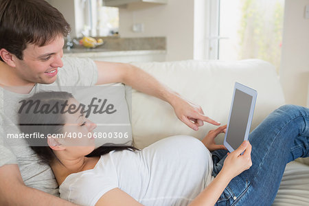 Young prospective parents lying on the couch while relaxing and using the tablet pc
