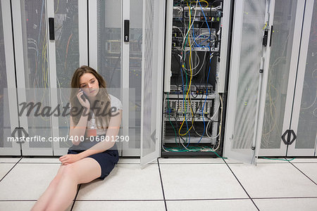 Woman sitting on the floor beside servers on the phone in data center