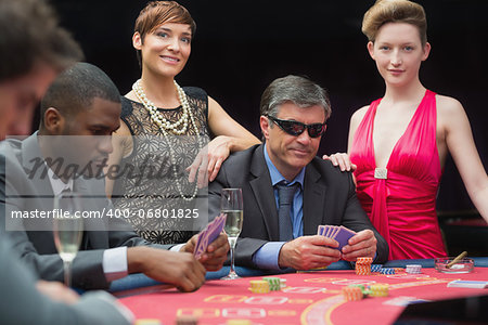 Man in sunglasses playing poker with two women either side in casino