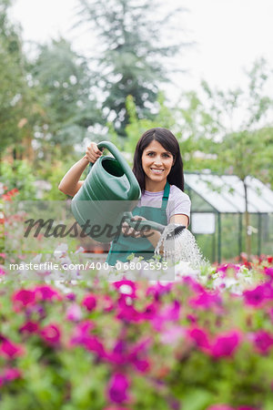 Cheerful woman working in garden center watering the plants outside