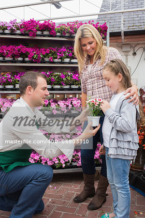 Employee giving a flower to little girl while her mother standing next to her in garden center